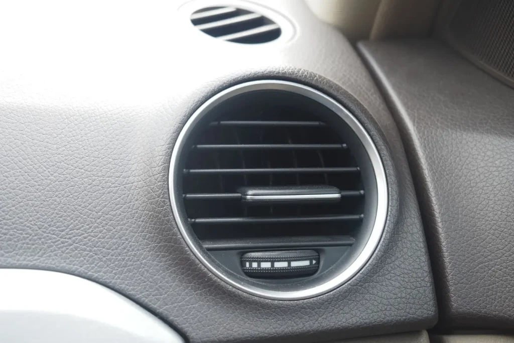 Vue rapprochée d’une bouche d’aération sur tableau de bord, contrôle visuel après recharge de climatisation voiture