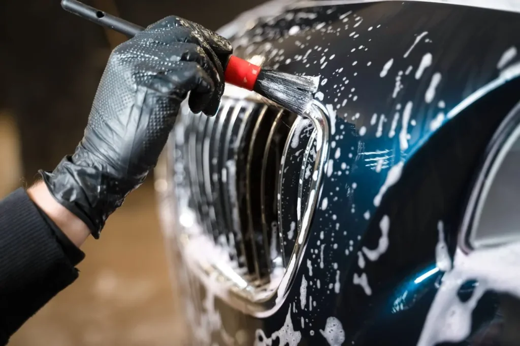 Main gantée utilisant un pinceau de detailing avec de la mousse pour éliminer la résine sur la carrosserie d'une voiture bleue