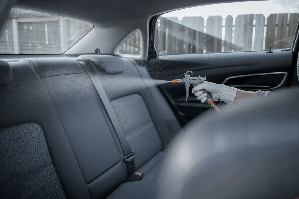 Un professionnel utilise un pistolet de nettoyage à vapeur sur les sièges arrière gris pour enlever l'odeur de tabac en voiture et purifier les tissus en profondeur.