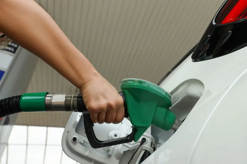 Une main tient un pistolet de carburant vert inséré dans le réservoir d'une voiture blanche illustrant l'importance de bien choisir son essence à la station