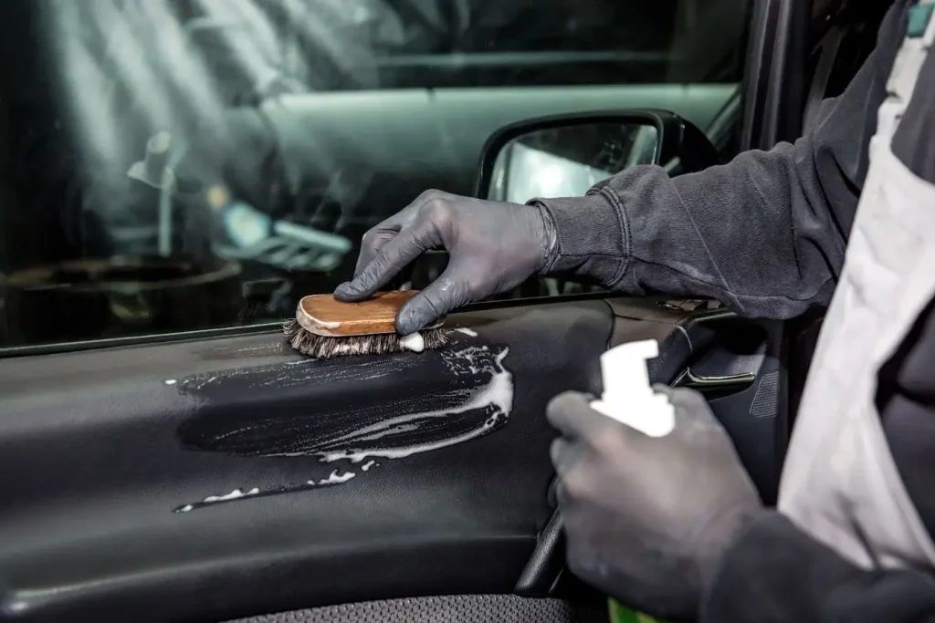 Personne en gants noirs nettoyant une portière avec mousse et brosse dans le cadre d’un polish voiture