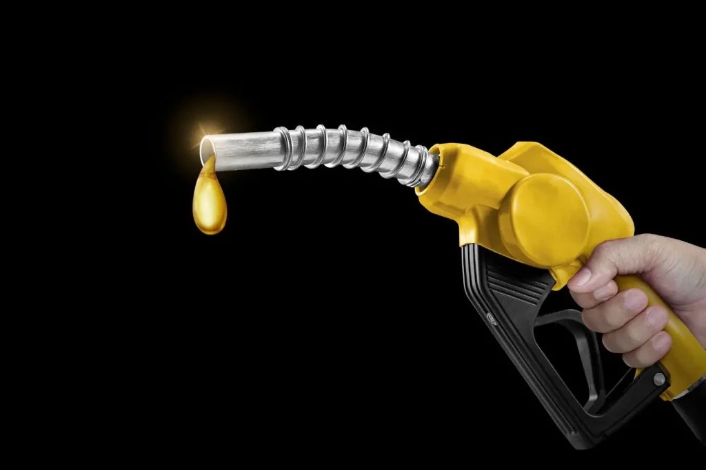 Une main tient un pistolet de pompe jaune sur fond noir d'où tombe une goutte dorée pour symboliser l'importance de bien choisir son essence pour son moteur