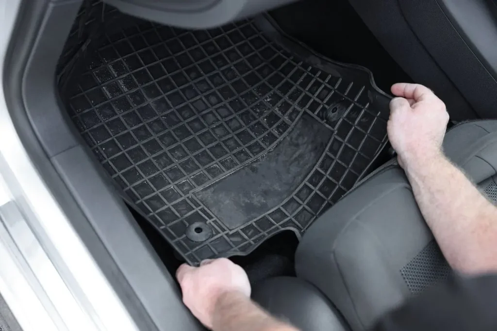Mains ajustant un tapis en caoutchouc dans l’habitacle illustrant une installation de protection intérieure