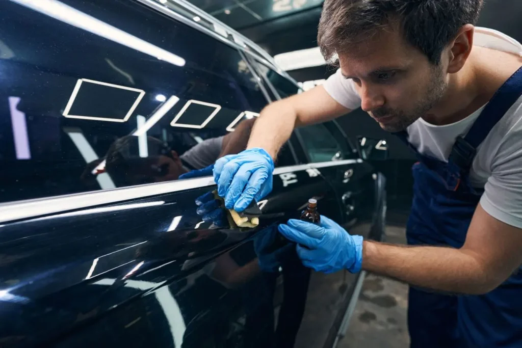 Spécialiste ganté appliquant avec soin un produit protecteur sur la carrosserie noire d'une berline pour un traitement céramique