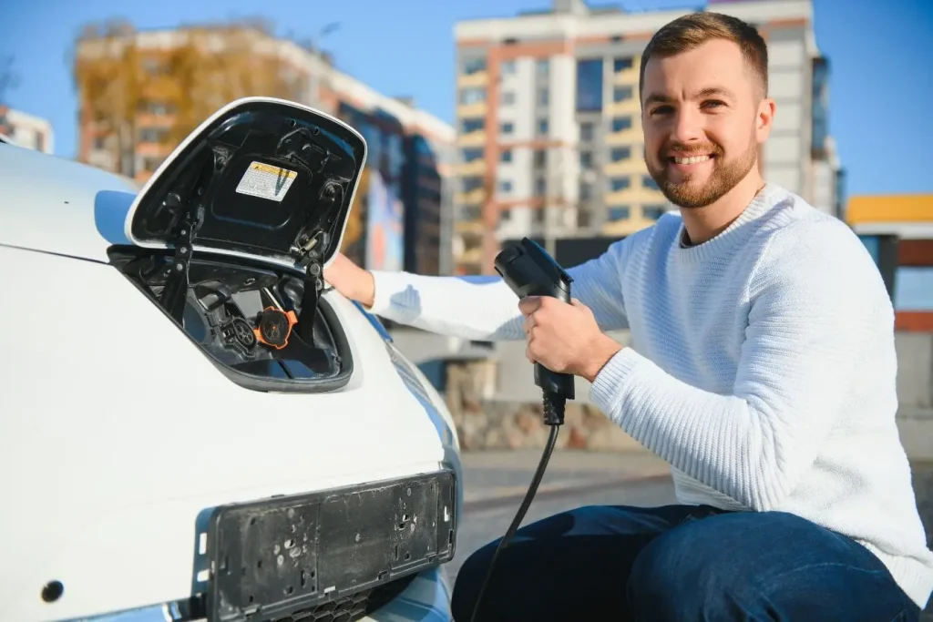 Personne tenant un câble devant une voiture électrique illustrant l’usage d’un chargeur intelligent pour batterie