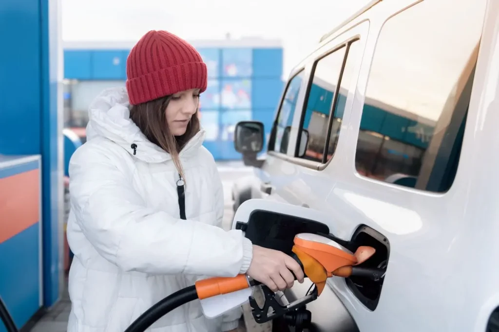 Personne en manteau blanc et bonnet rouge fait le plein, image illustrant le Diesel B10 et son usage quotidien.