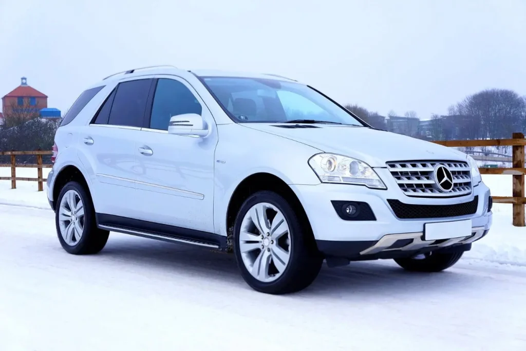 SUV blanc Mercedes stationné sur route enneigée, équipé d’un marche-pied électrique facilitant l’accès avec confort et sécurité