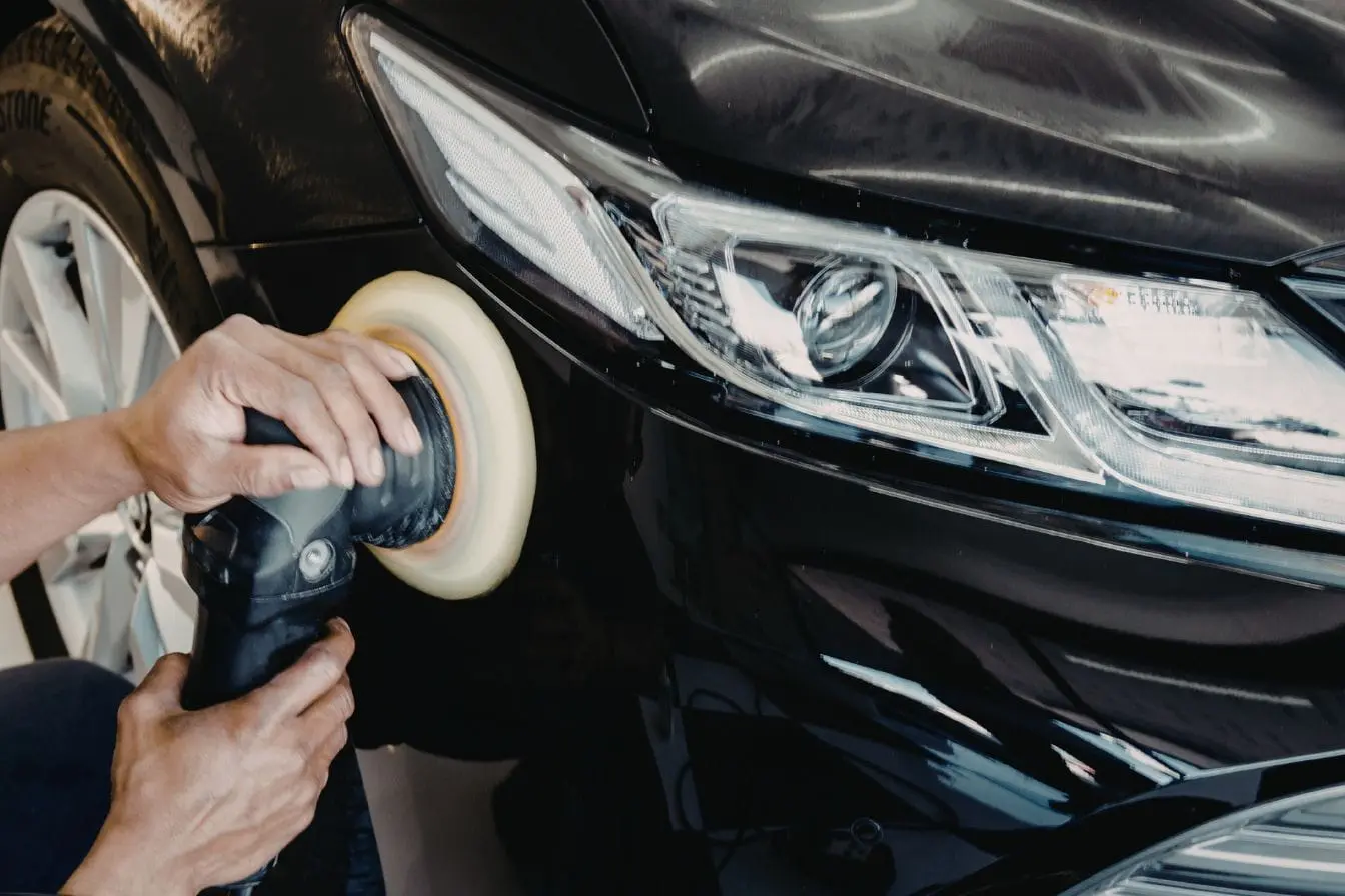 carrosserie Gros plan sur mains utilisant polisseuse électrique sur aile de voiture noire brillante, illustrant l’application de cire de carrosserie pour éclat et protection