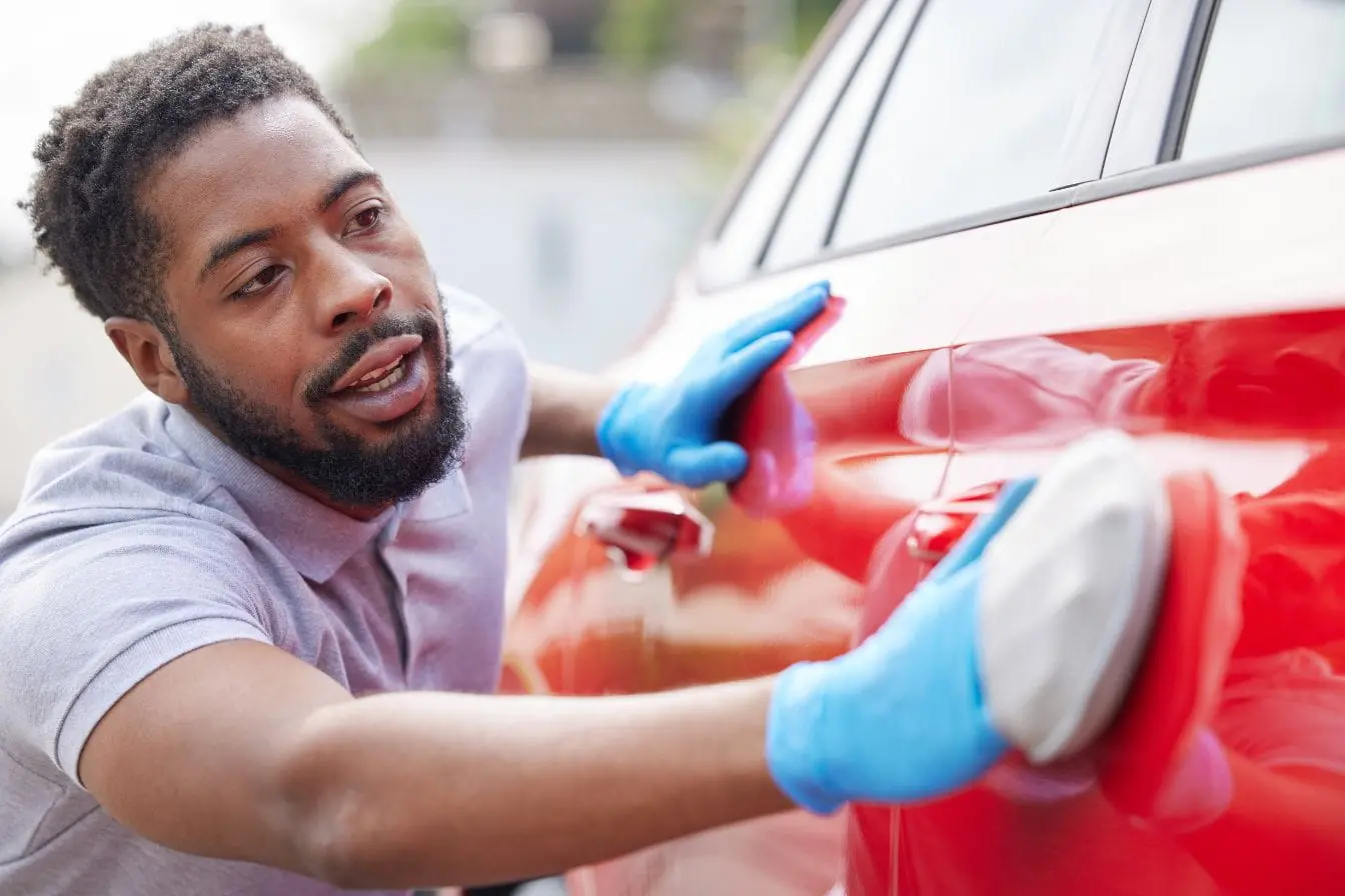 carrosserie Personne polissant une voiture rouge illustrant l’application de vernis carrosserie pour protéger et sublimer l’éclat de la peinture