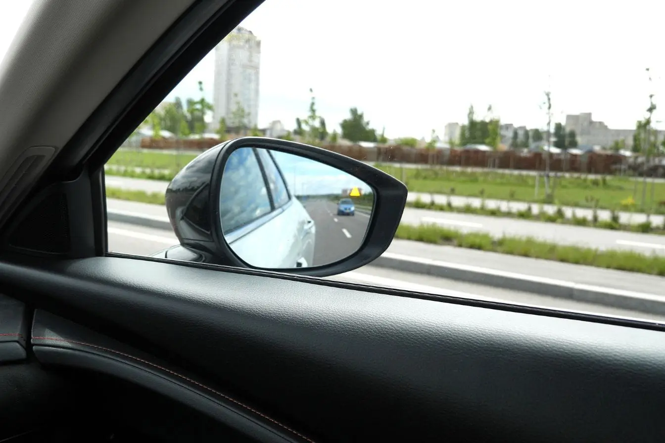 détection d’angle mort Vue d’un rétroviseur latéral montrant une voiture approchant dans la voie adjacente illustrant l’importance de la détection d’angle mort en conduite