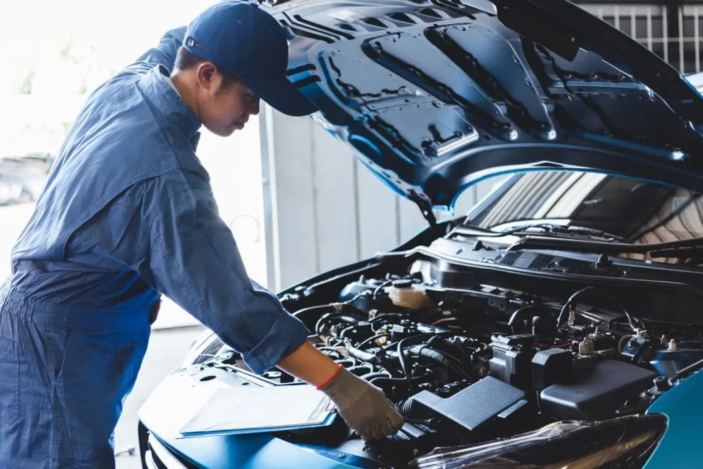 Mécanicien en uniforme bleu inspecte compartiment moteur ouvert, image illustrant l’action de nettoyer son moteur pour entretien automobile