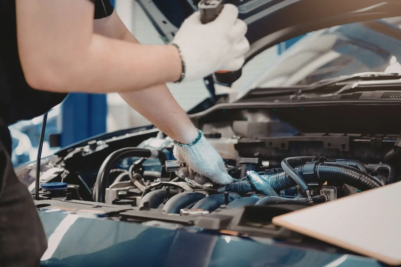 Gros plan sur un mécanicien en gants blancs travaillant dans le compartiment moteur, image illustrant l’action de nettoyer son moteur pour entretien