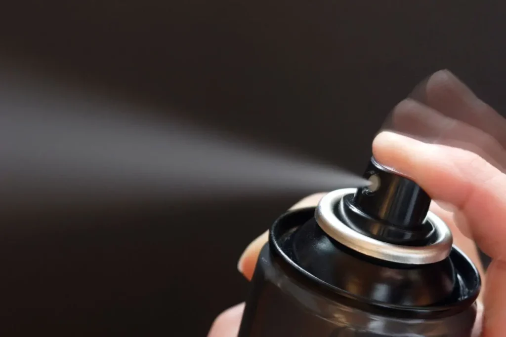 Main appuyant sur bombe aérosol illustrant l’application de vernis carrosserie pour protéger et sublimer la brillance de la peinture automobile