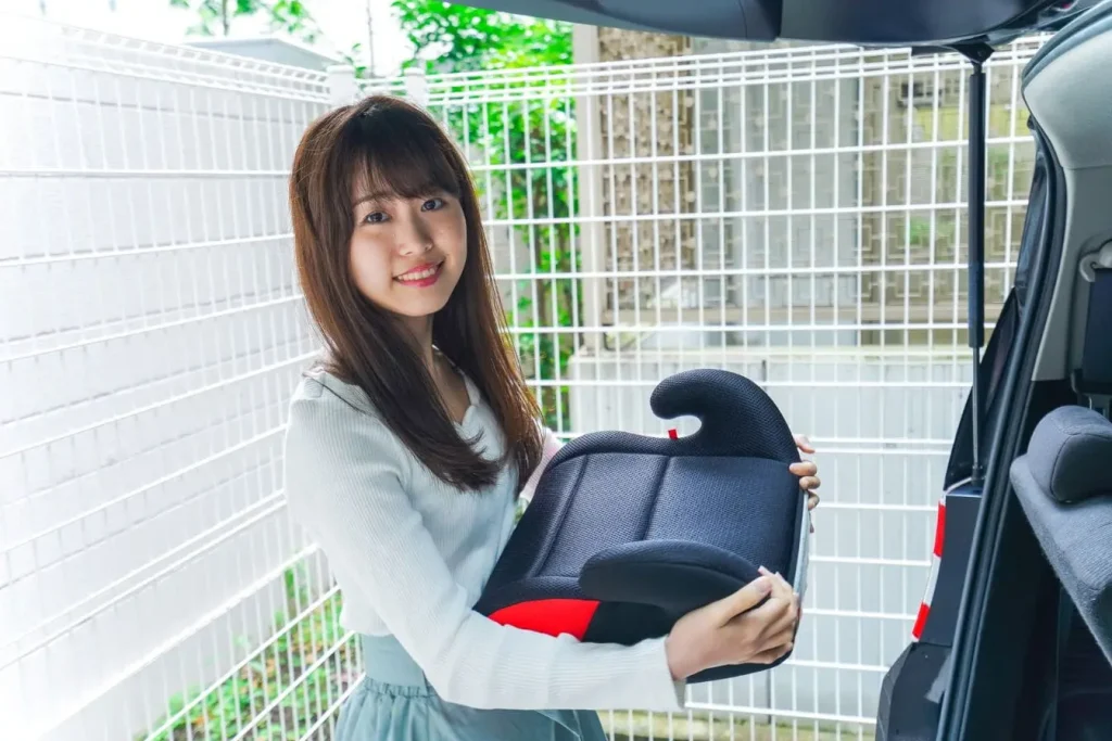 Femme tenant un réhausseur siège auto compact et léger avec des accoudoirs confortables