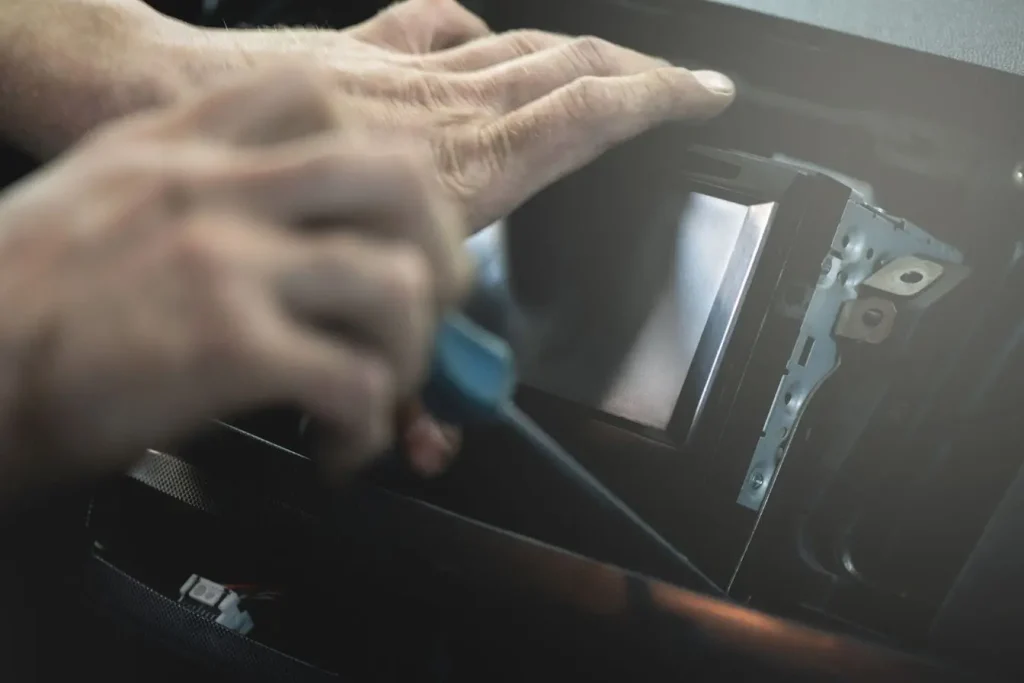 Gros plan sur mains retirant autoradio du tableau de bord, image illustrant réparation et installation de système audio embarqué en voiture.