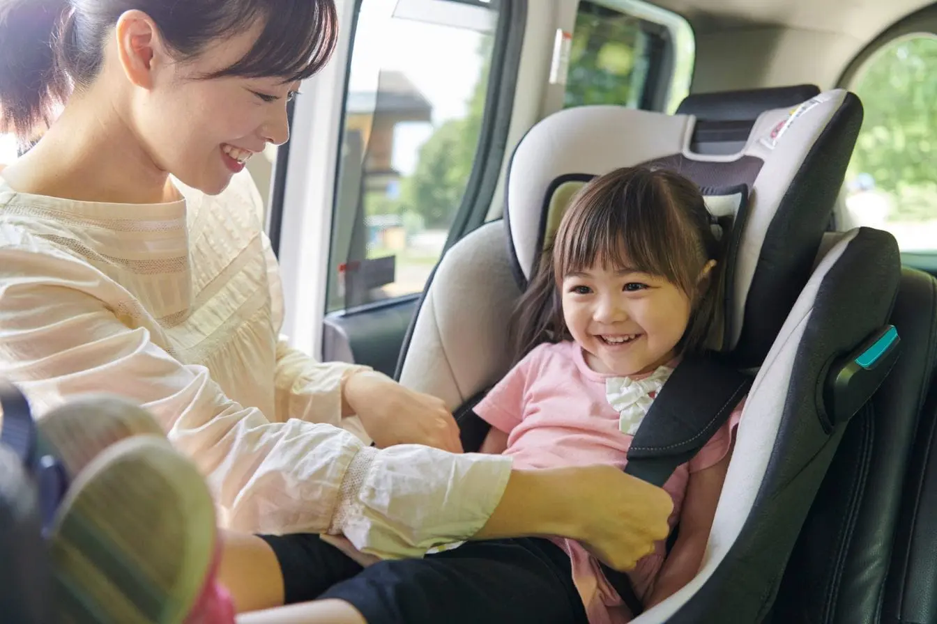 siège auto moderne Une maman souriante attache soigneusement la ceinture de sécurité de sa petite fille installée confortablement dans un siège auto moderne et sécurisé à l'arrière