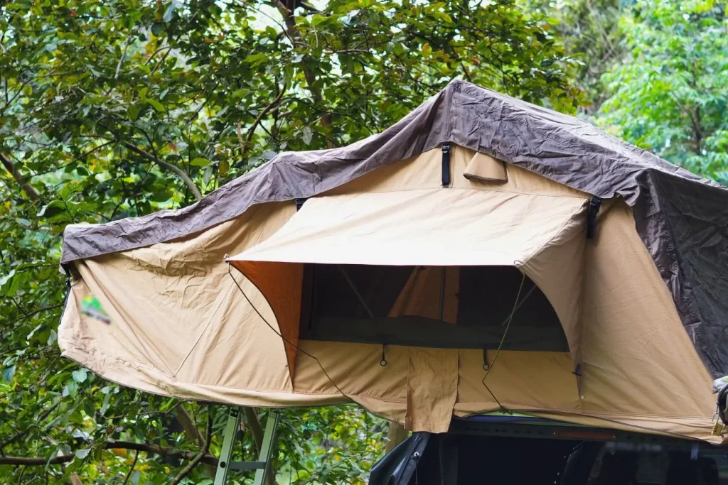 Voiture garée en forêt avec tente de toit beige et marron déployée, illustrant la pratique d’installer une tente de toit sur sa voiture pour camping