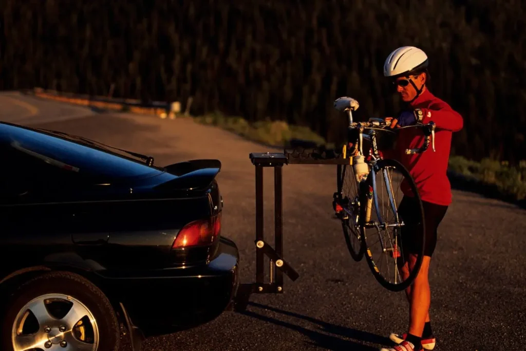 Cycliste en casque blanc chargeant vélo sur porte-vélo arrière d’une voiture noire, illustrant la praticité du porte-vélo pour sorties sportives