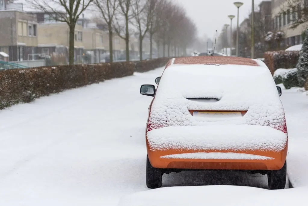 Voiture stationnée sous la neige, carrosserie exposée aux risques du sel hivernal, nécessité d’entretien préventif.