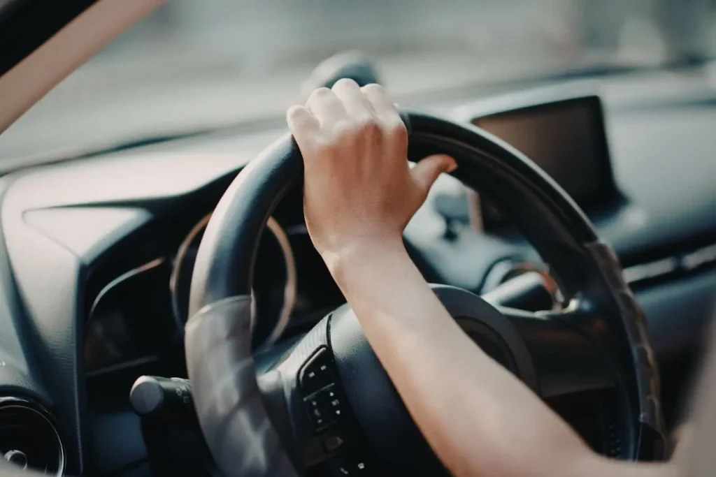 Main tenant le haut du volant d’une voiture illustrant l’usage d’une housse chauffante pour plus de confort thermique en conduite hivernale