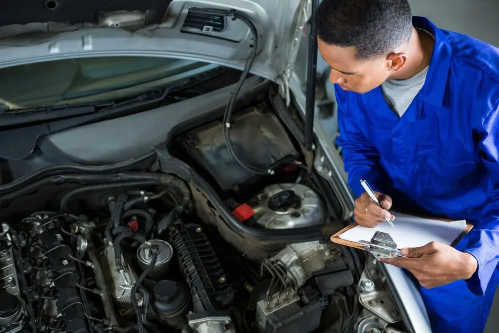 Mécanicien en uniforme bleu inspectant moteur avec carnet, image illustrant le calcul du bonus-malus lié à l’entretien automobile