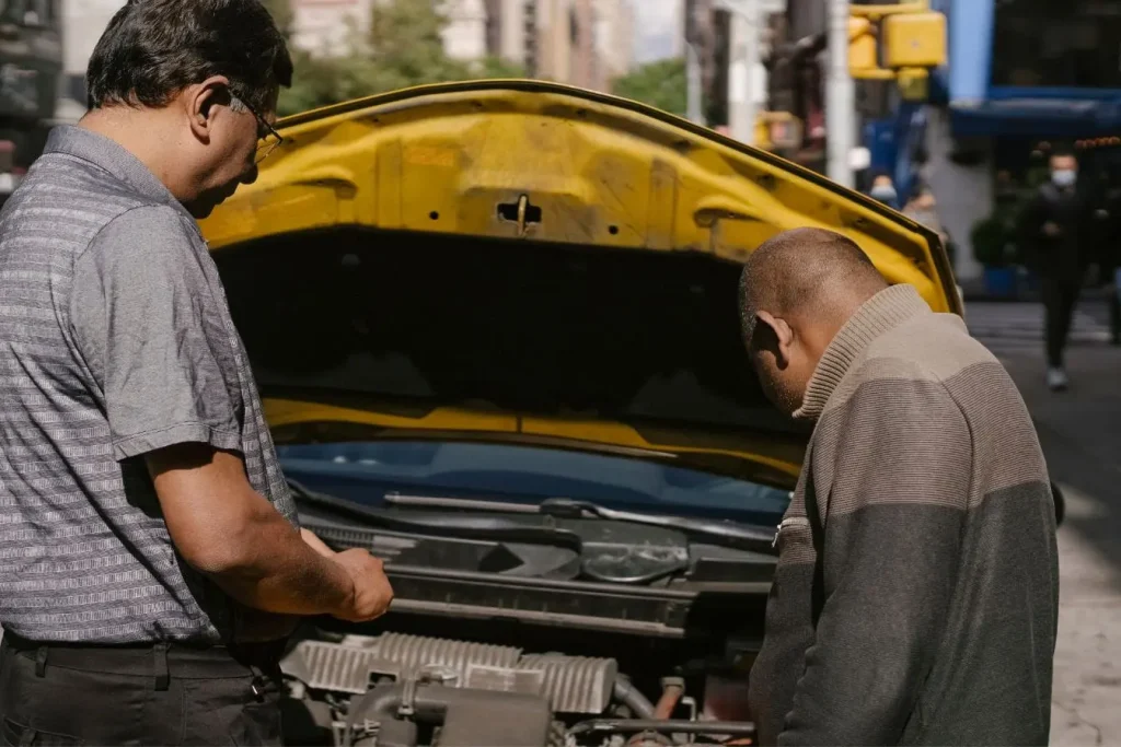 Deux personnes inspectent moteur d’une voiture capot ouvert en pleine rue, image évoquant la vigilance et le recours pour vice caché en cas de défaut mécanique.