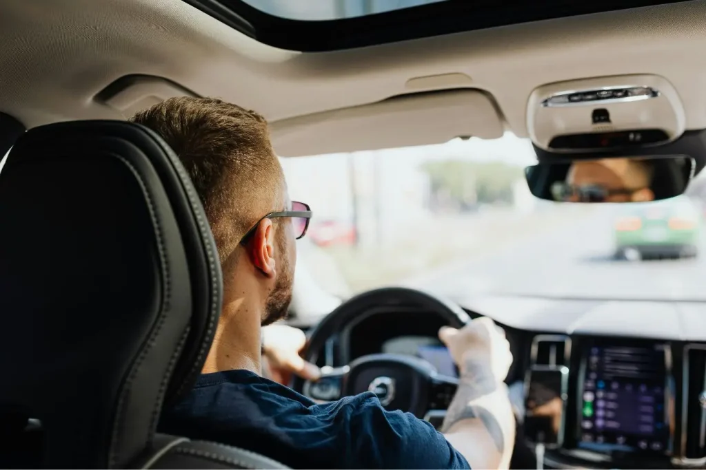 Un homme de dos conduit une voiture moderne sur une route ensoleillée