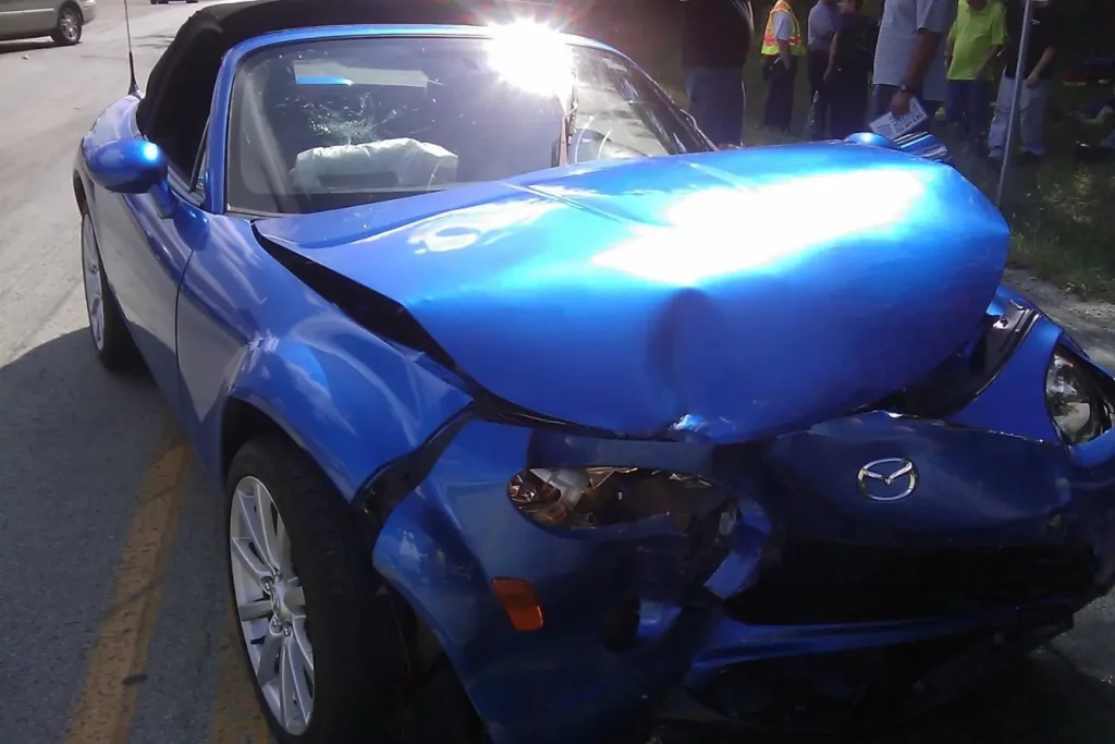 Photo d'une voiture bleue déformée après une collision frontale avec capot plié et pare-brise étoilé. Une situation critique pour déclarer un sinistre auto complet.