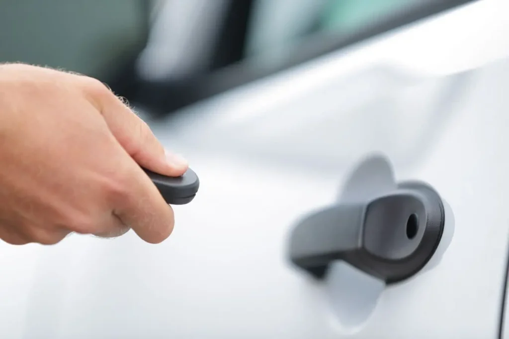 Main tenant une télécommande noire pour activer un démarreur à distance fraîchement installé sur une voiture blanche afin de préchauffer le moteur en hiver