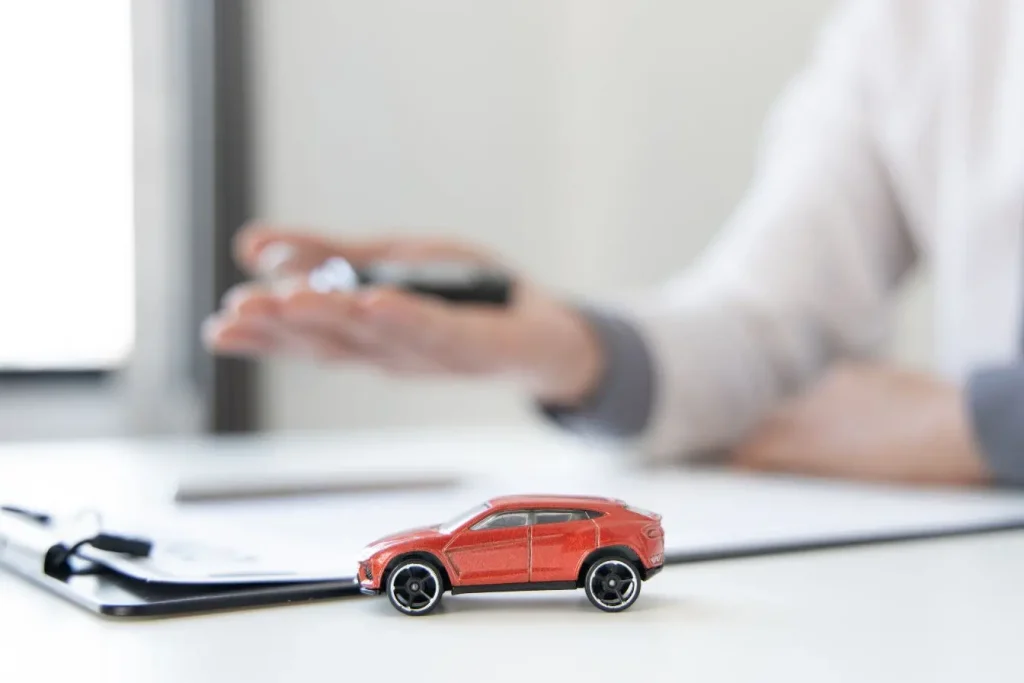 Petite voiture rouge sur documents, image illustrant la différence entre assurance auto au tiers limitée et assurance tous risques couvrant tous dommages.
