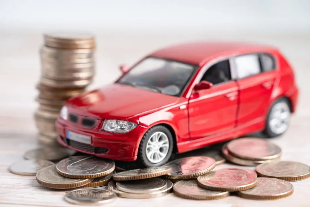 Petite voiture rouge posée sur pièces de monnaie, image illustrant la résiliation d’une assurance auto et la gestion des coûts liés au véhicule.