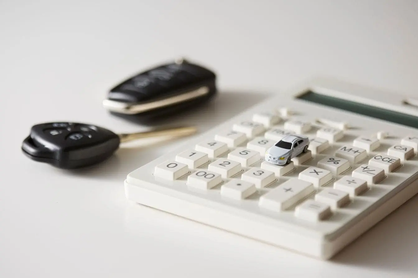 calcul du bonus-malus Calculatrice blanche avec petite voiture posée sur touches et clés noires à côté, image illustrant le calcul du bonus-malus automobile.