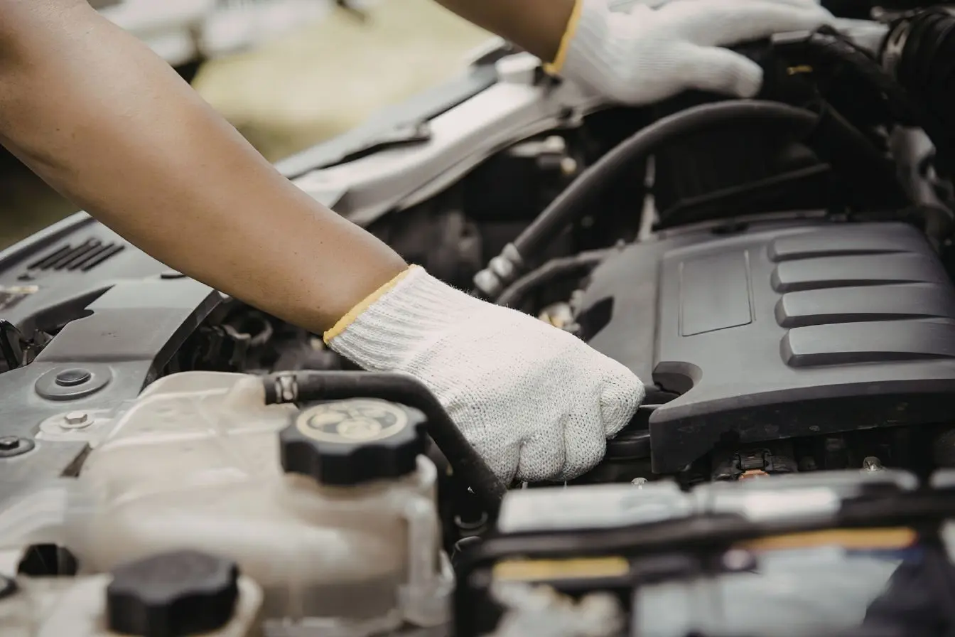 compartiment moteur Mécanicien ajuste des pièces dans un compartiment moteur avec gants de protection, image illustrant l’importance de la protection du carter moteur