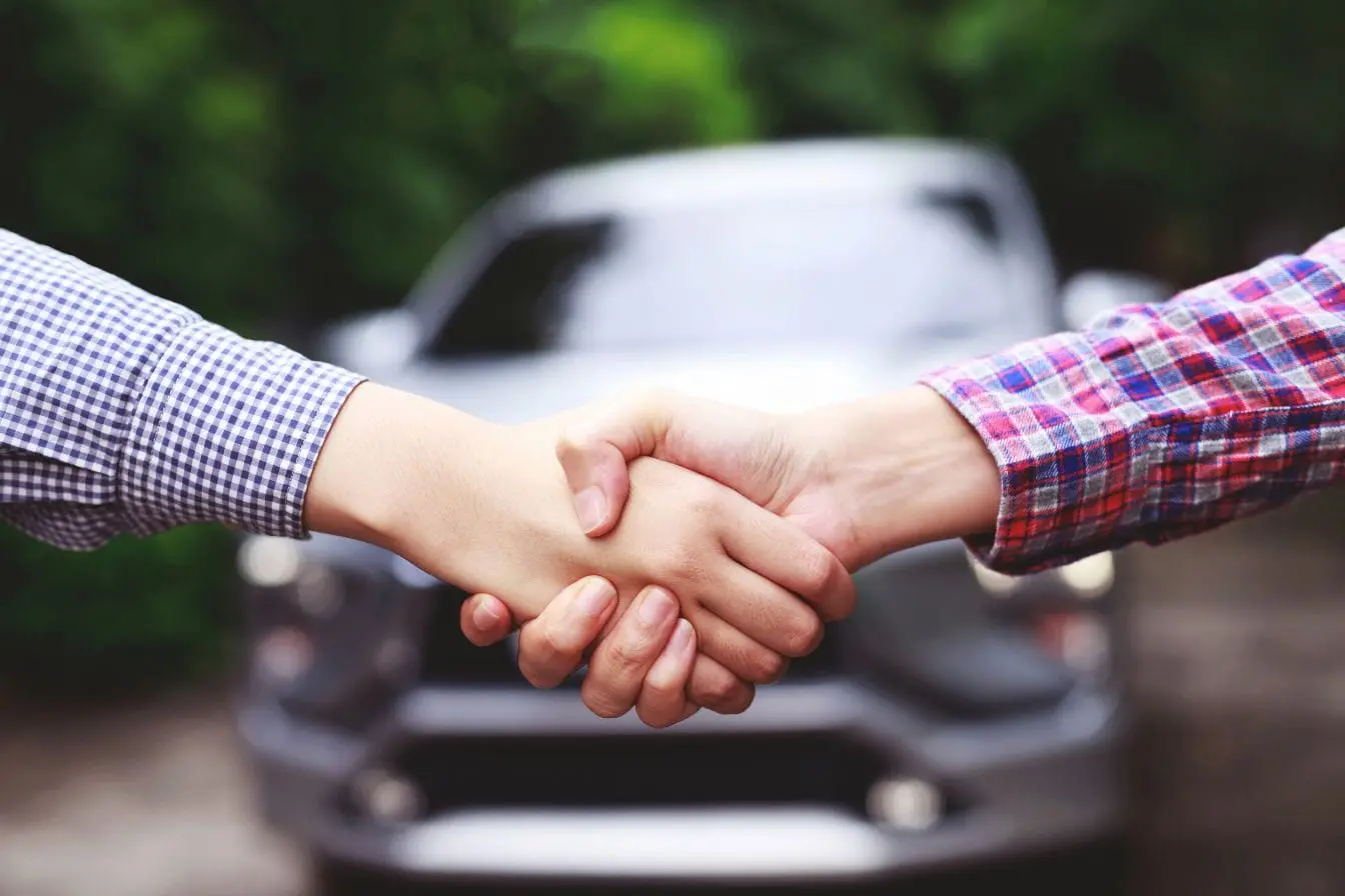 contrat LOA Deux personnes se serrent la main devant une voiture, image illustrant un accord de LOA où le client loue avec option d’achat.