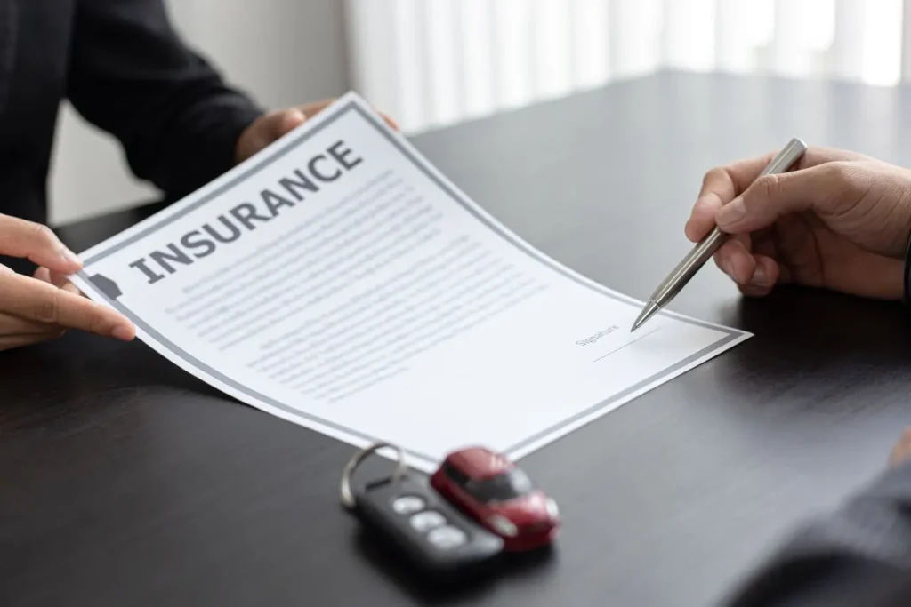 Une personne s'apprête à signer un document d'assurance avec une voiture miniature et des clés à côté. Une étape clé pour déclarer un sinistre auto officiellement.