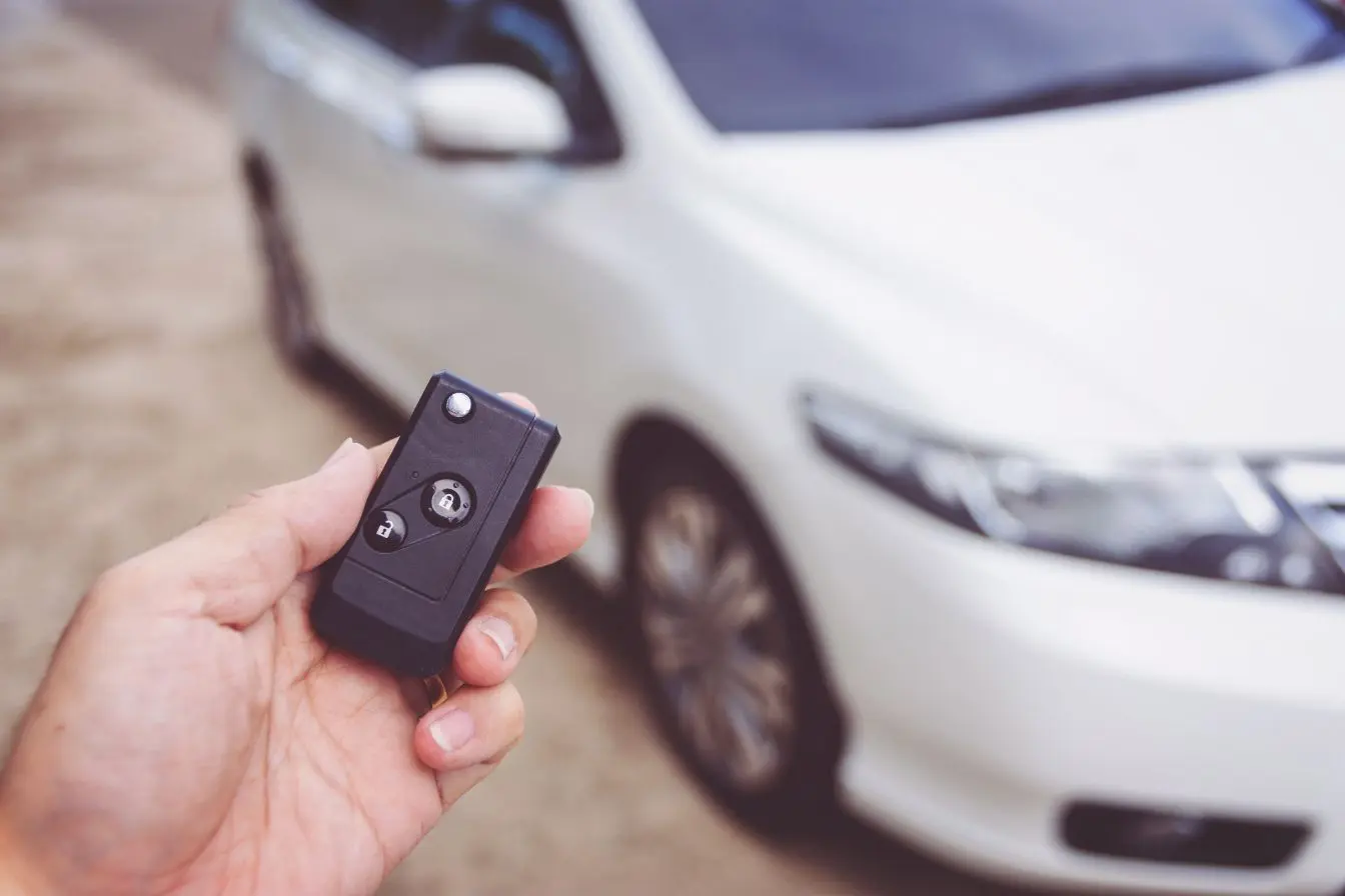 Main tenant une télécommande noire pour utiliser un démarreur à distance sur une voiture blanche stationnée à l'extérieur pour un confort thermique optimal