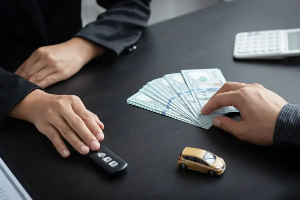 Transaction avec billets de cent dollars échangés contre clés de voiture, image illustrant la franchise en assurance auto et le coût à la charge du conducteur.