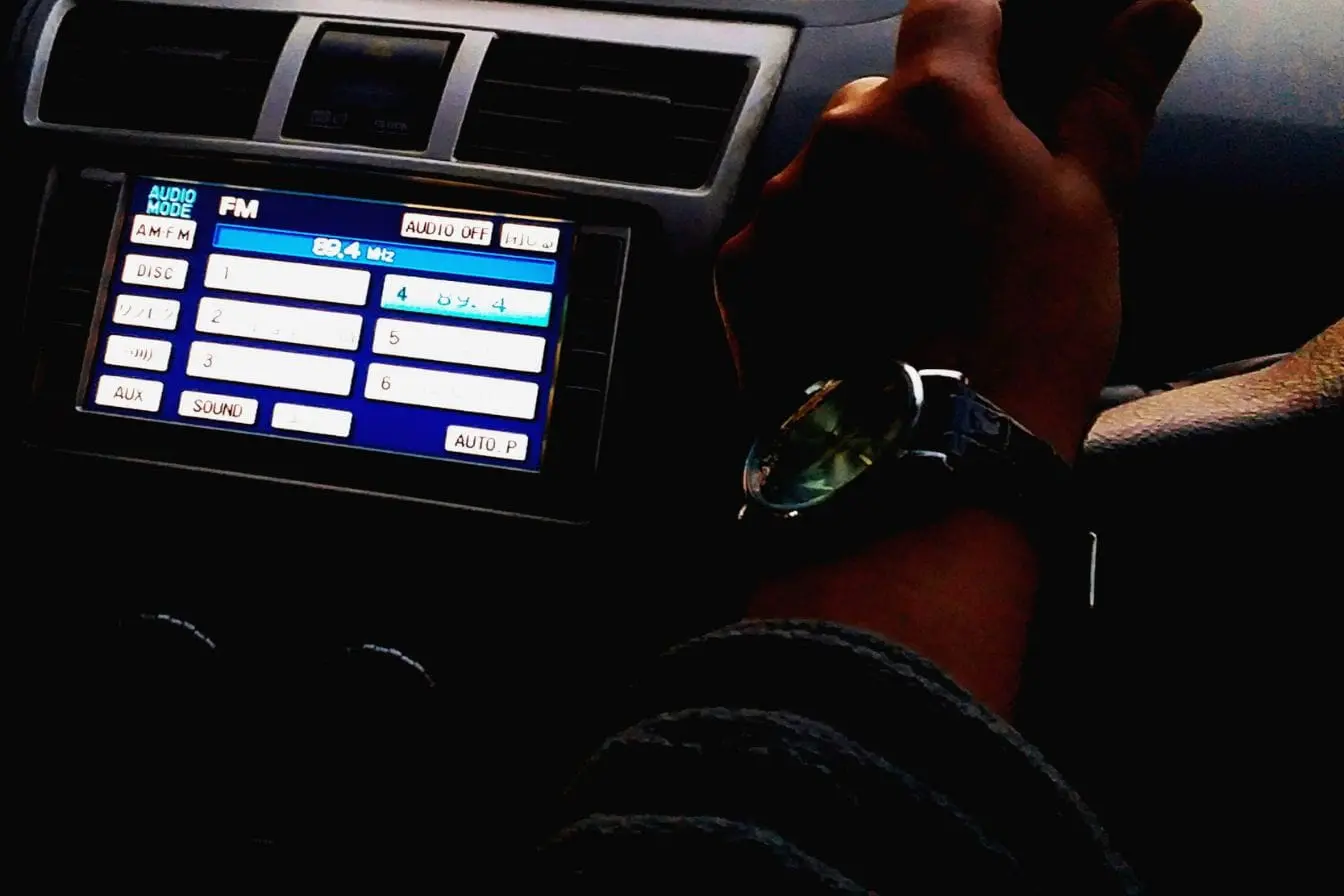 installer un autoradio Autoradio numérique tactile fraîchement installé dans le tableau de bord d'une voiture affichant la fréquence FM 89.4 MHz sous la main du conducteur au volant.