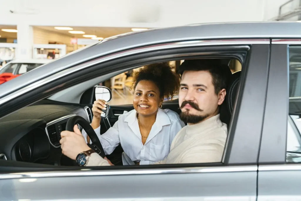 Conducteur souriant tenant le volant avec passager brandissant des clés, image illustrant la réussite et la récupération des points de permis.