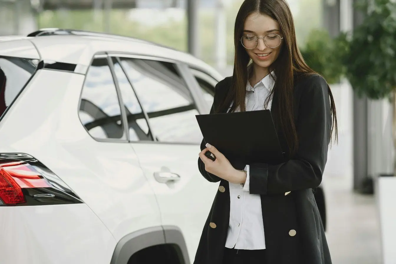 rédaction d’un constat amiable Personne en tenue professionnelle tenant un dossier près d’un SUV blanc, image illustrant la rédaction d’un constat amiable après un incident routier.