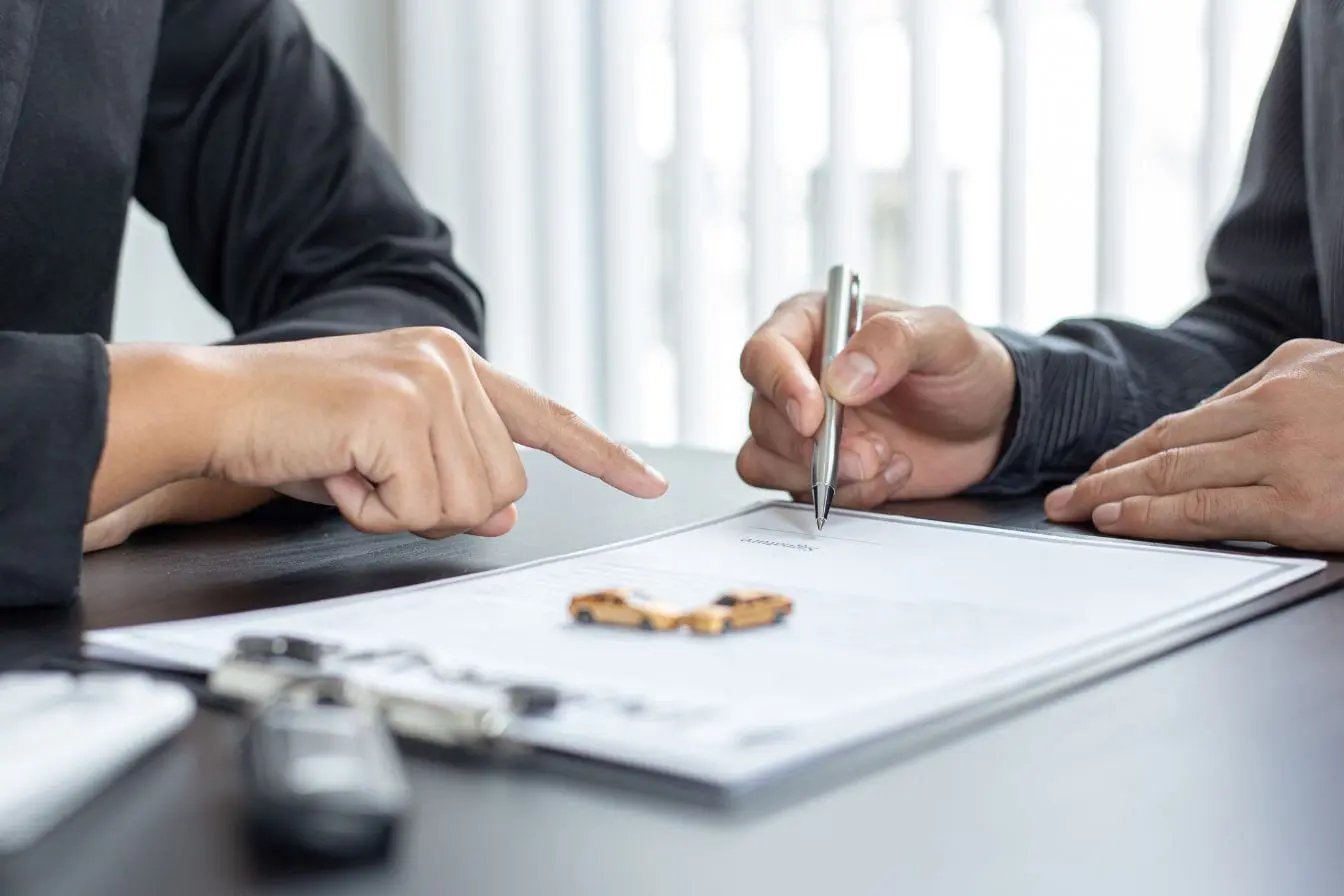 résiliation d’assurance auto Deux personnes assises signant un document avec clés de voiture sur bureau, image illustrant la résiliation d’une assurance auto.