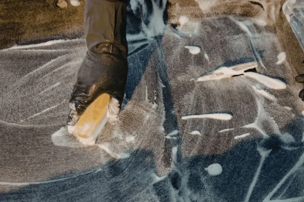 Main gantée frottant une surface savonneuse avec une brosse illustrant l’action d’enlever des autocollants collés sur une voiture