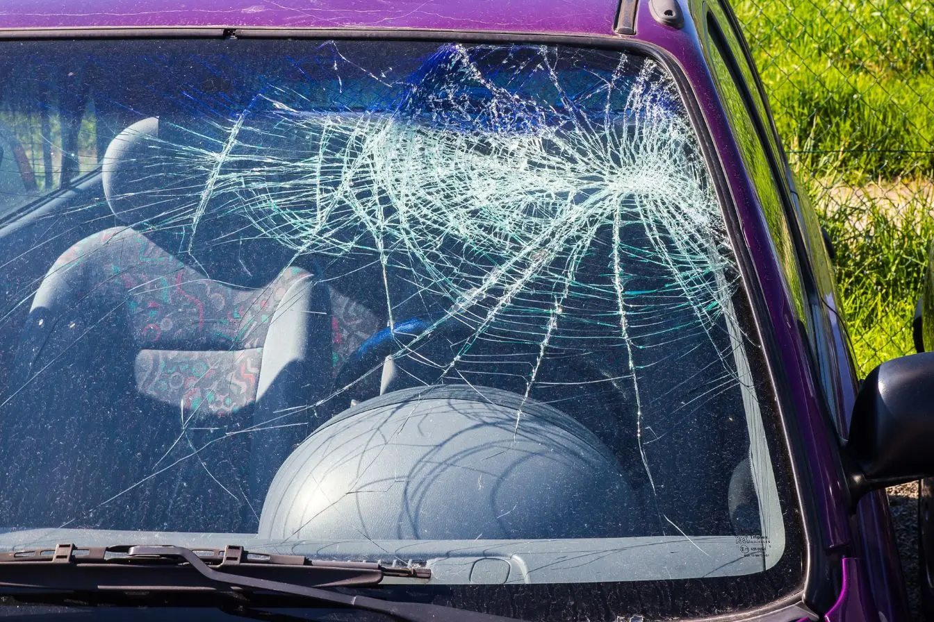 Gros plan sur un pare-brise de voiture violette totalement étoilé et brisé suite à un accident.