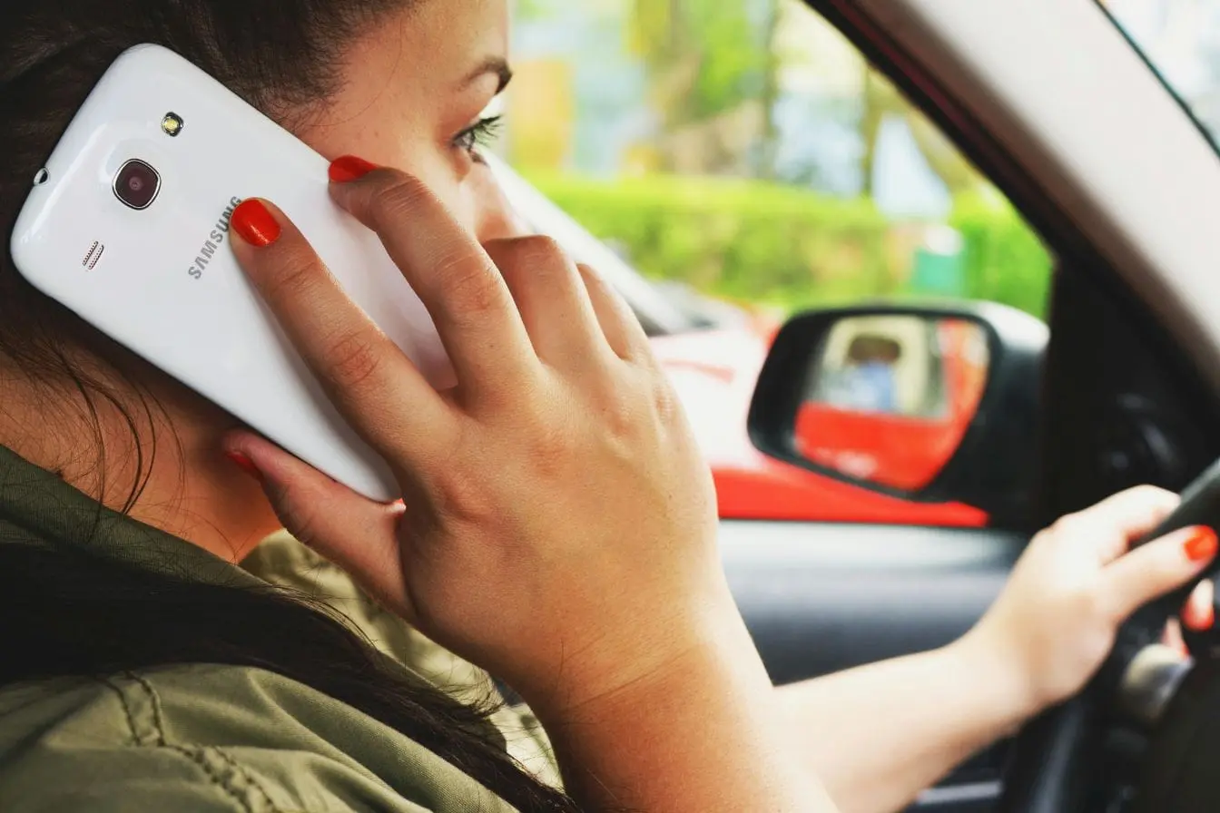 Personne au volant Conductrice tenant smartphone à l’oreille en conduisant, image illustrant le téléphone au volant et les sanctions prévues avec retrait de points en 2026.