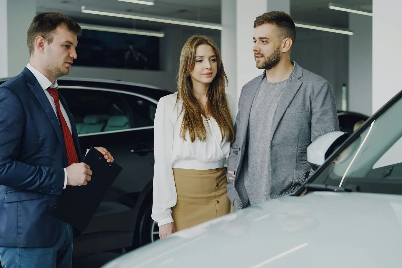 achat d’une voiture Client en couple face à vendeur en costume avec voiture claire, image d’une négociation de prix pour l’achat d’une voiture