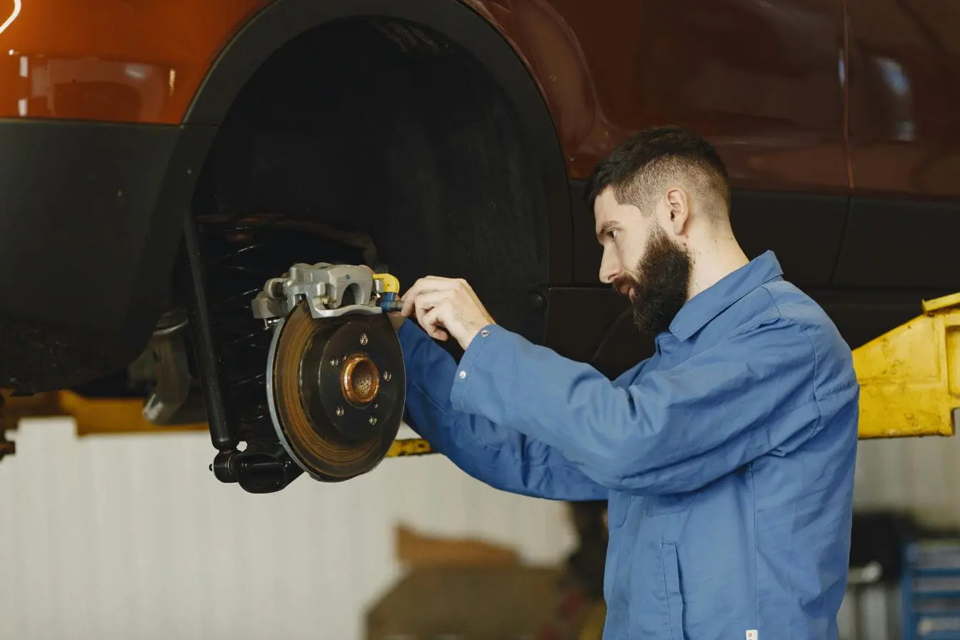 disque Mécanicien en bleu ajustant étrier de frein sur voiture levée, image illustrant le changement des plaquettes de frein pour assurer sécurité routière.