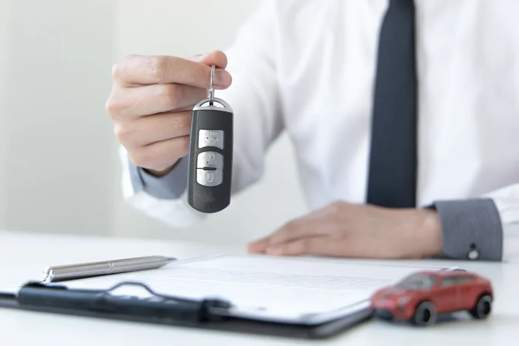Main tenant clé de voiture au-dessus d’un document signé, reflet d’une transaction après négociation du prix.