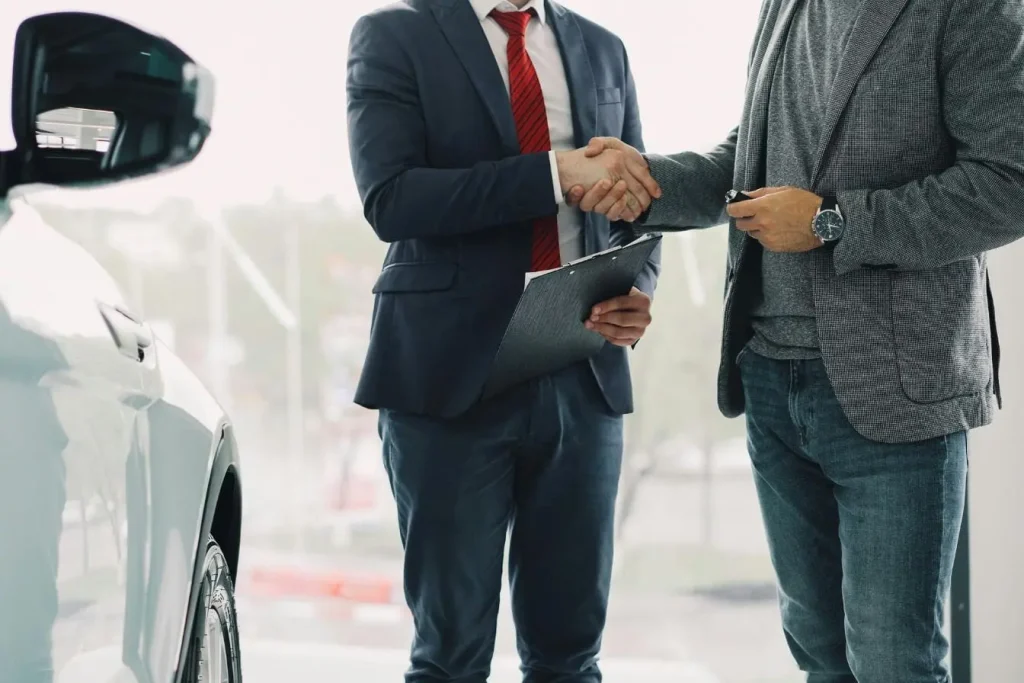 Acheteur tenant clé de voiture face à vendeur avec dossier, reflet d’une transaction où le prix a été discuté.