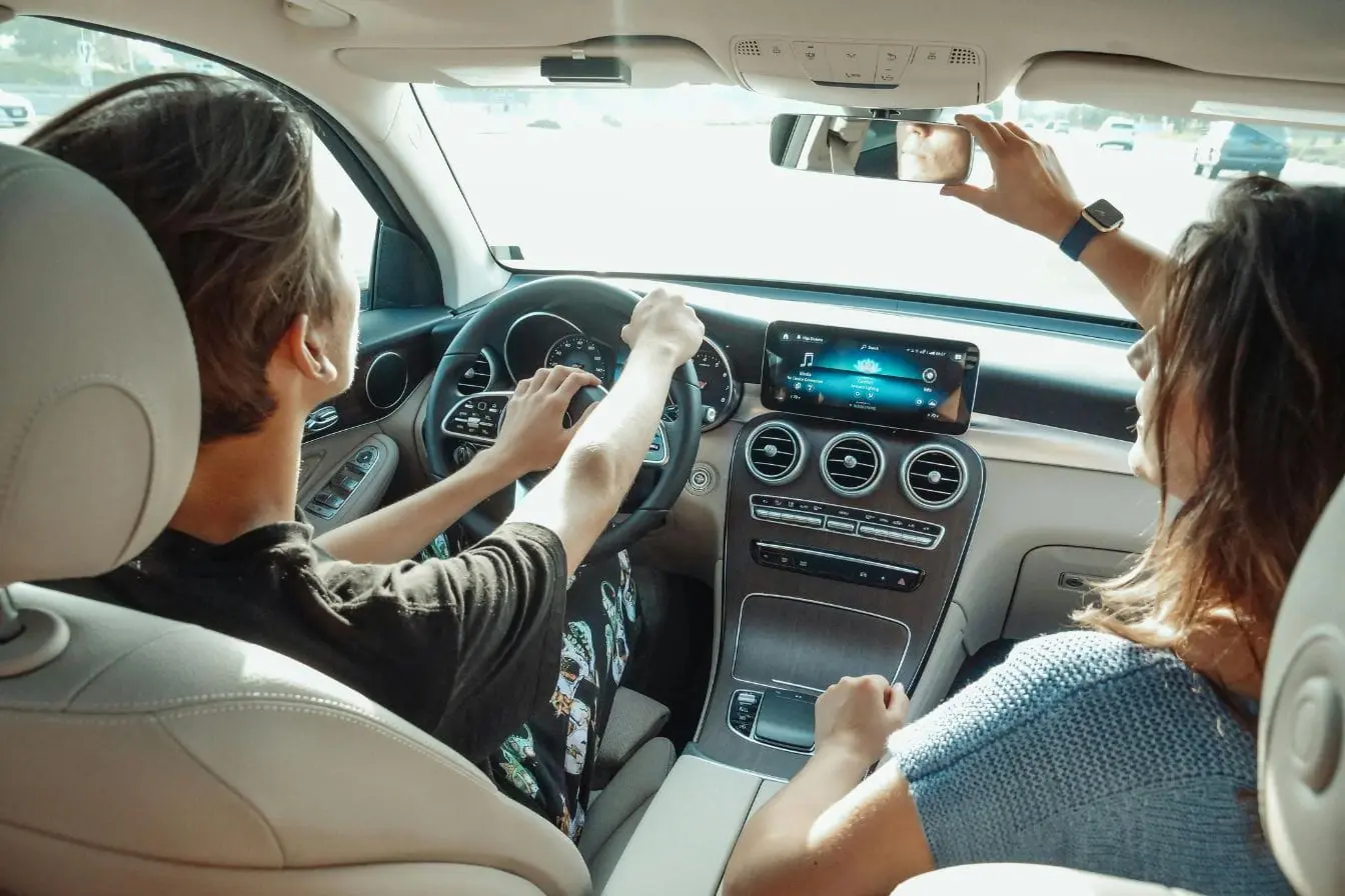 passer du permis auto au manuel Conducteur tenant le volant avec passager ajustant miroir, image illustrant la transition du permis auto au manuel et l’apprentissage pratique.