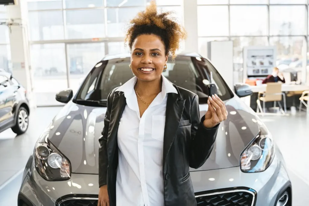 Personne tenant clé devant voiture grise dans showroom lumineux